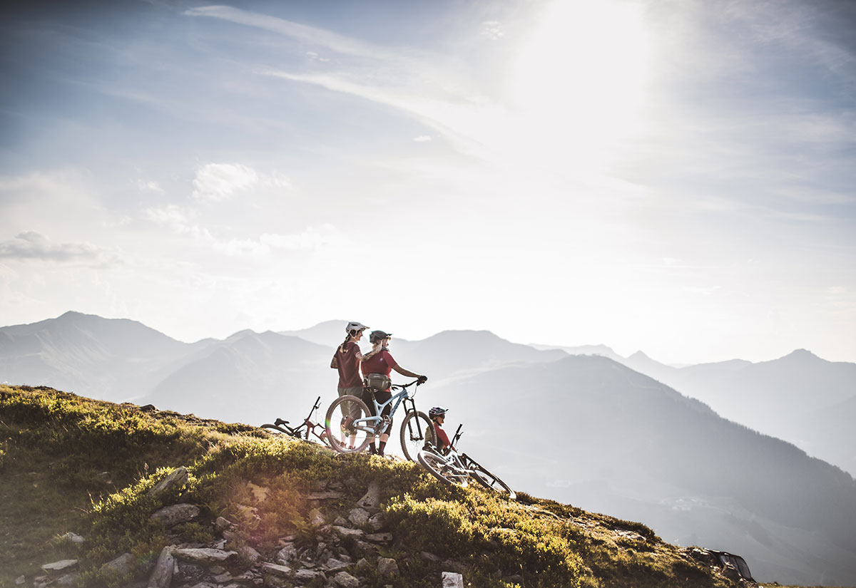 Drei Mountainbiker stehen auf einem Hügel und blicken in die schöne Berglandschaft von Saalbach Hinterglemm.