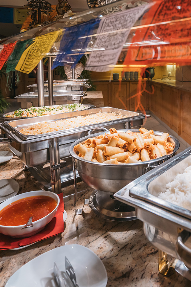 Buffetbereich mit einer Auswahl an Gerichten, darunter Frühlingsrollen, Reis und eine Schale mit Sauce